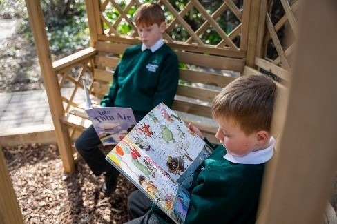 Two pupils reading together in a wooden garden shelter
