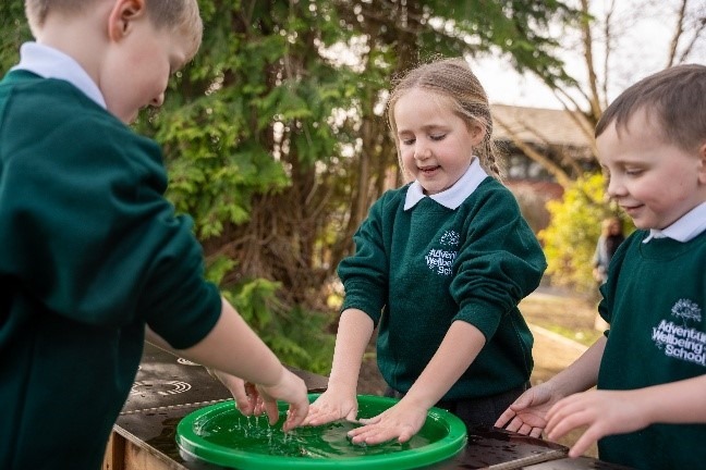 Three pupils in green school jumpers playing at a water tray outdoors